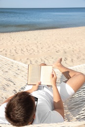 Photo of Young man reading book in hammock on beach