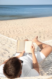 Young man reading book in hammock on beach