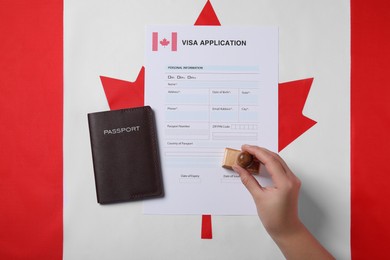 Photo of Immigration to Canada. Woman stamping visa application form on flag, top view