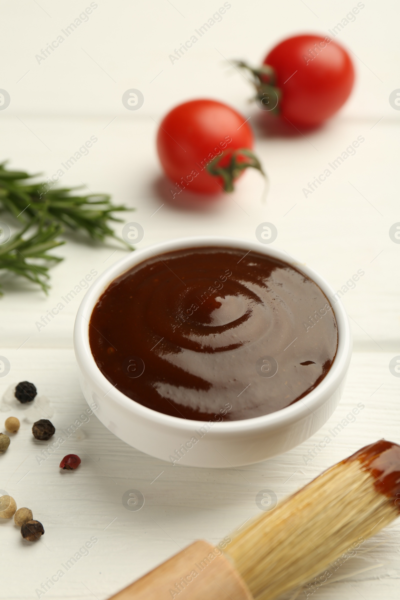 Photo of Tasty barbeque sauce in bowl, rosemary and spices on white wooden table