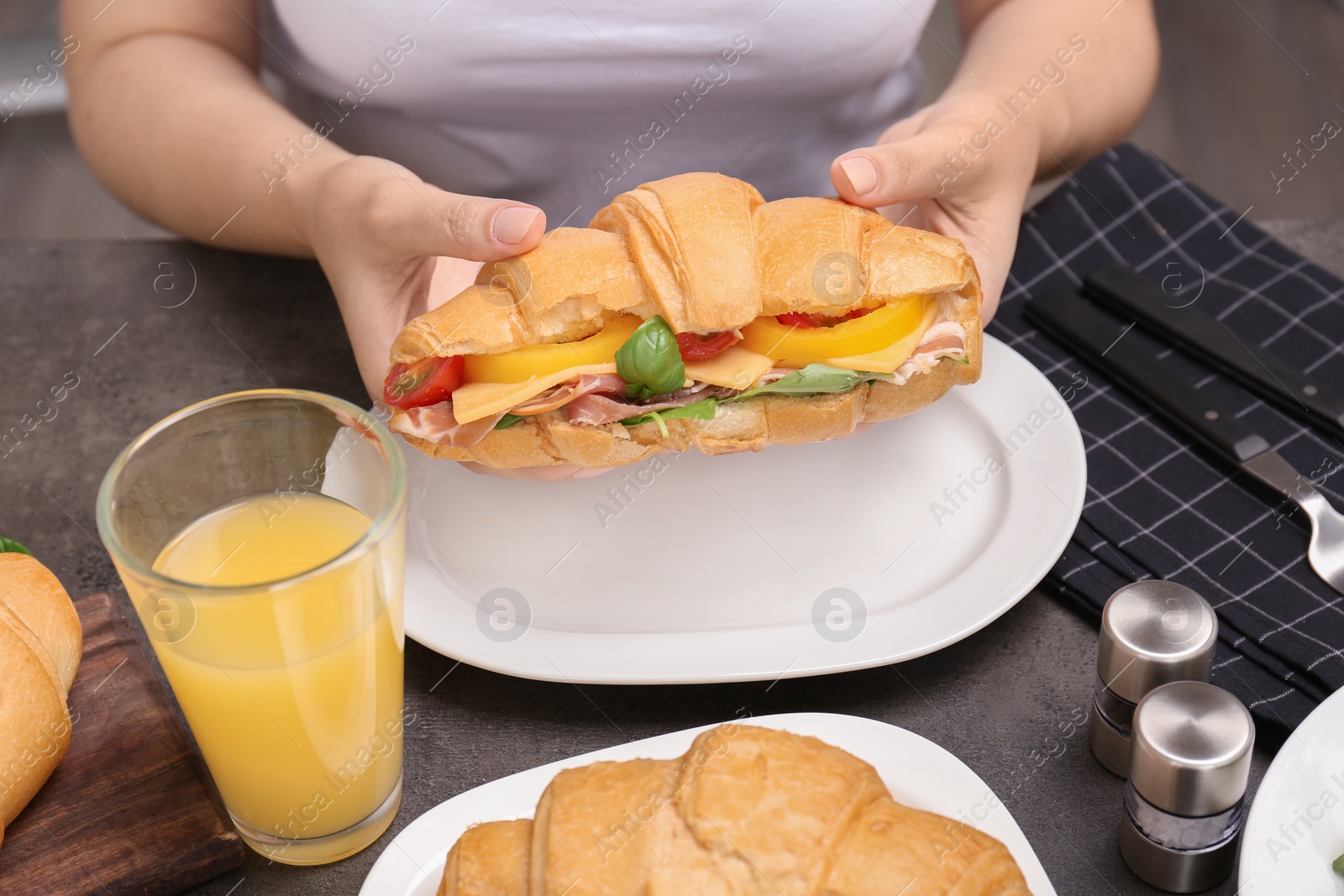 Photo of Woman holding tasty croissant sandwich over plate at table