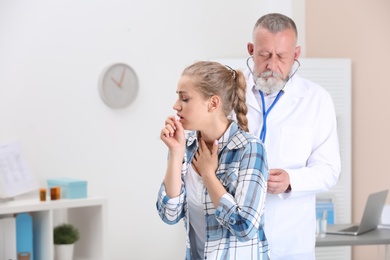 Doctor examining coughing young woman at clinic