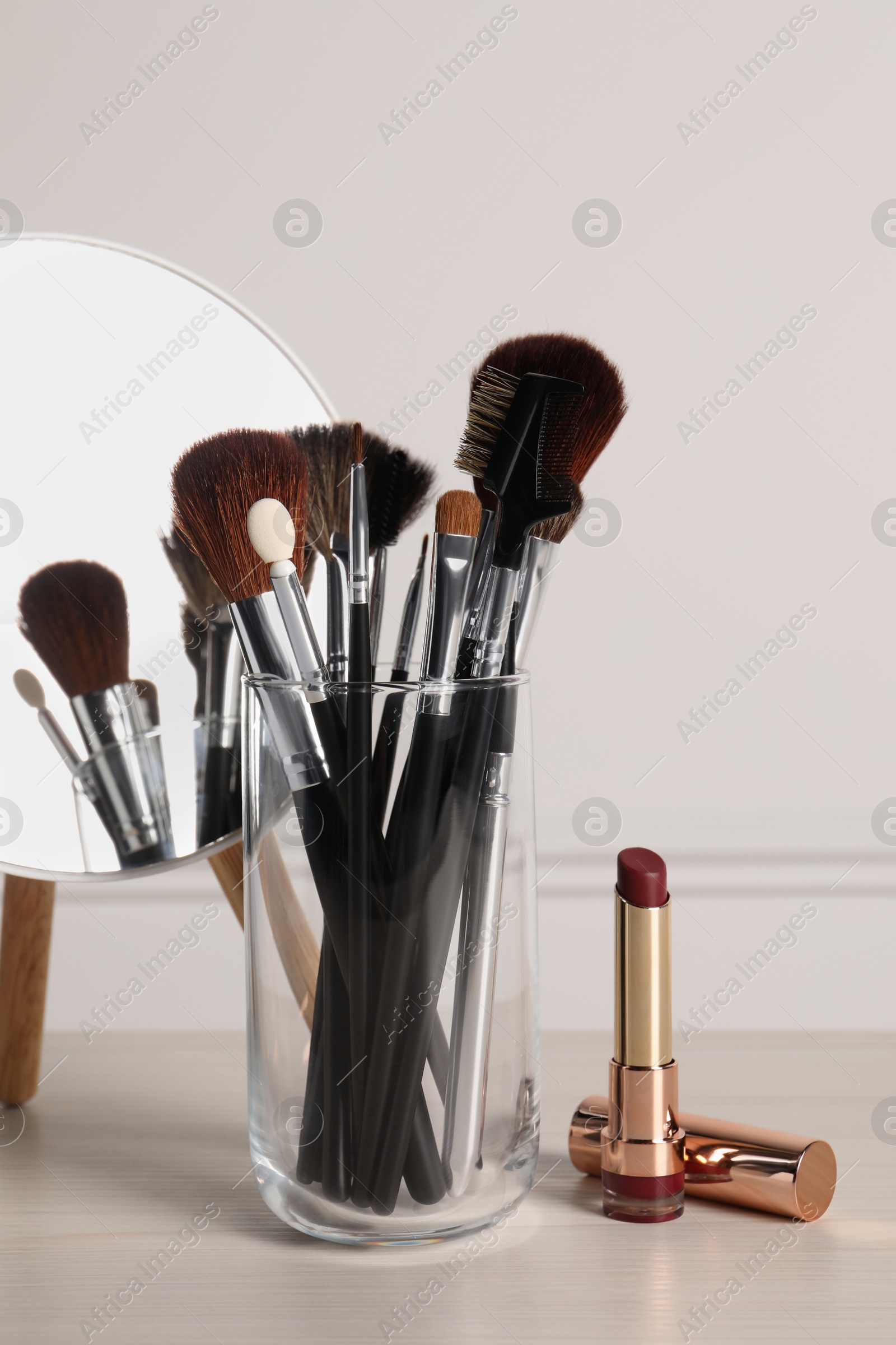 Photo of Set of professional brushes, lipstick and mirror on wooden table