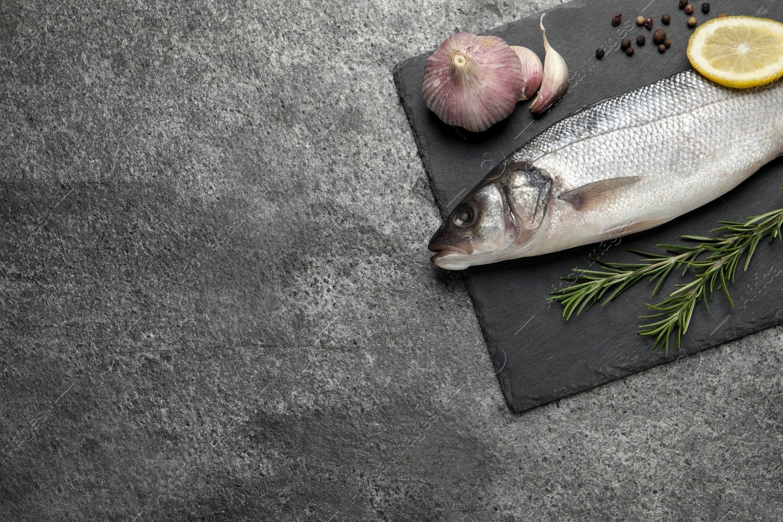 Photo of Sea bass fish and ingredients on grey table, top view. Space for text