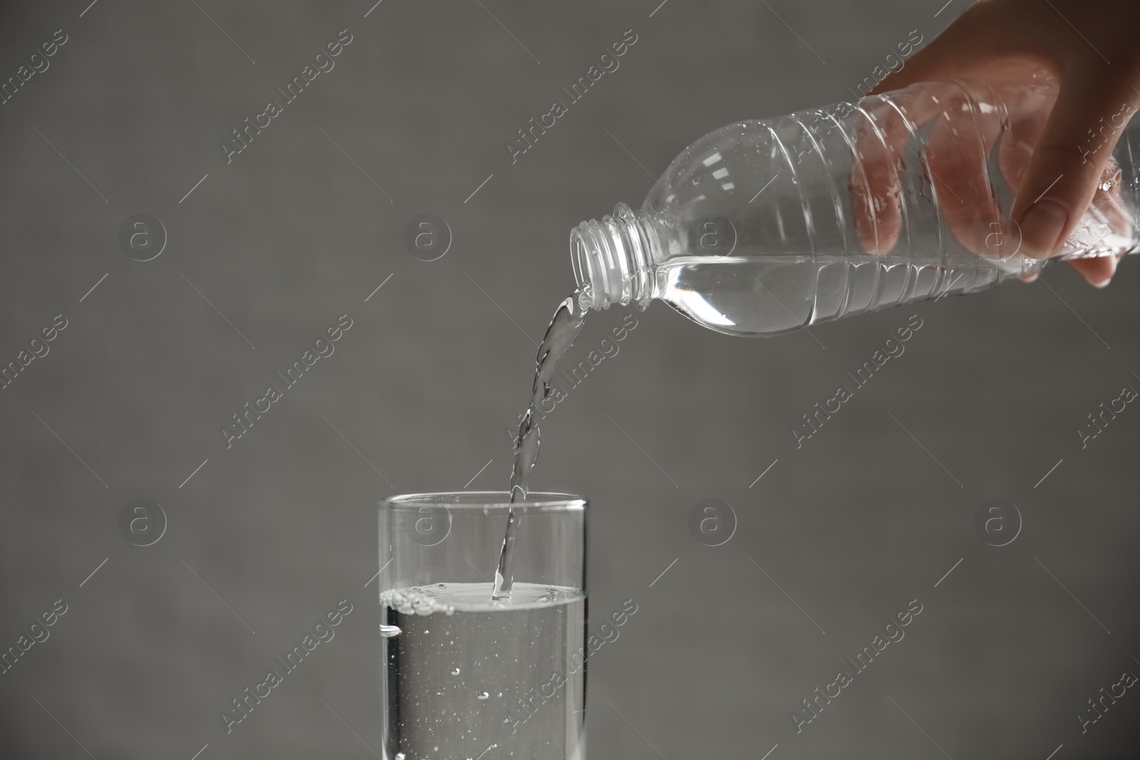 Photo of Woman pouring water from bottle into glass against blurred background, closeup