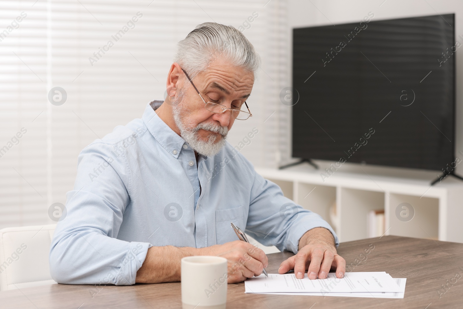 Photo of Senior man signing Last Will and Testament at wooden table indoors