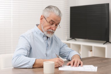 Photo of Senior man signing Last Will and Testament at wooden table indoors