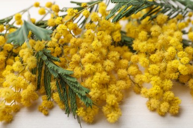 Photo of Beautiful mimosa flowers on white wooden table, closeup