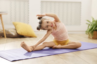 Photo of Little cute girl stretching herself on mat at home