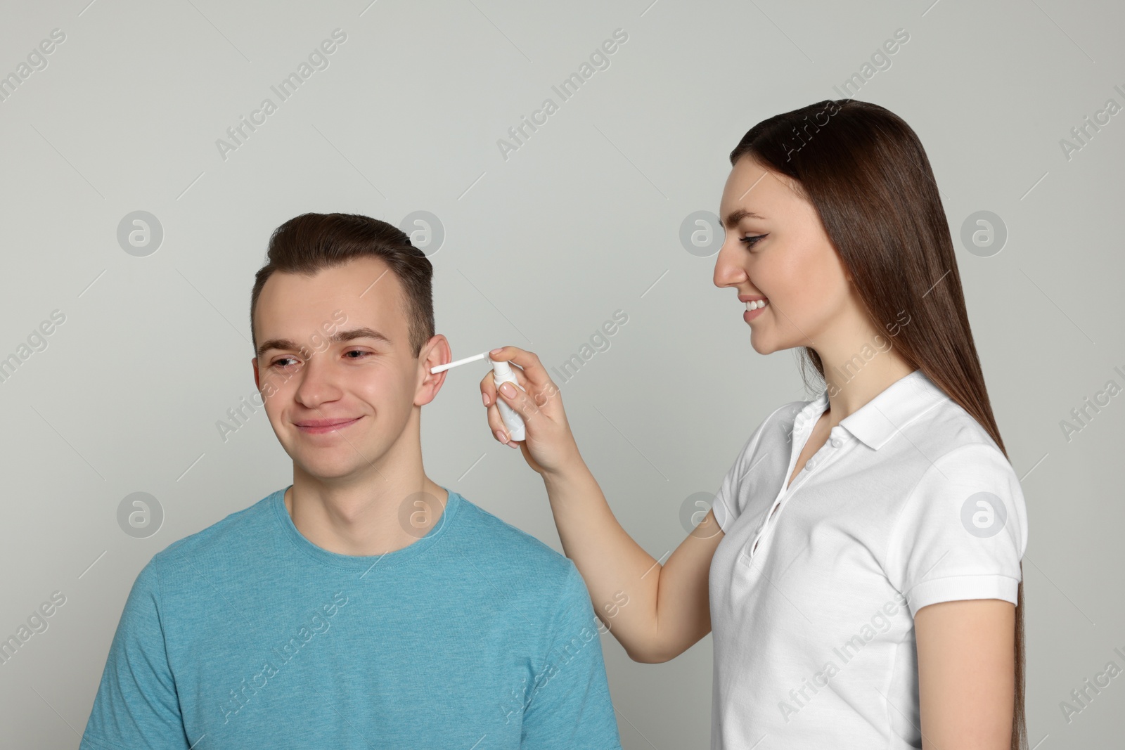 Photo of Woman spraying medication into man`s ear on light grey background