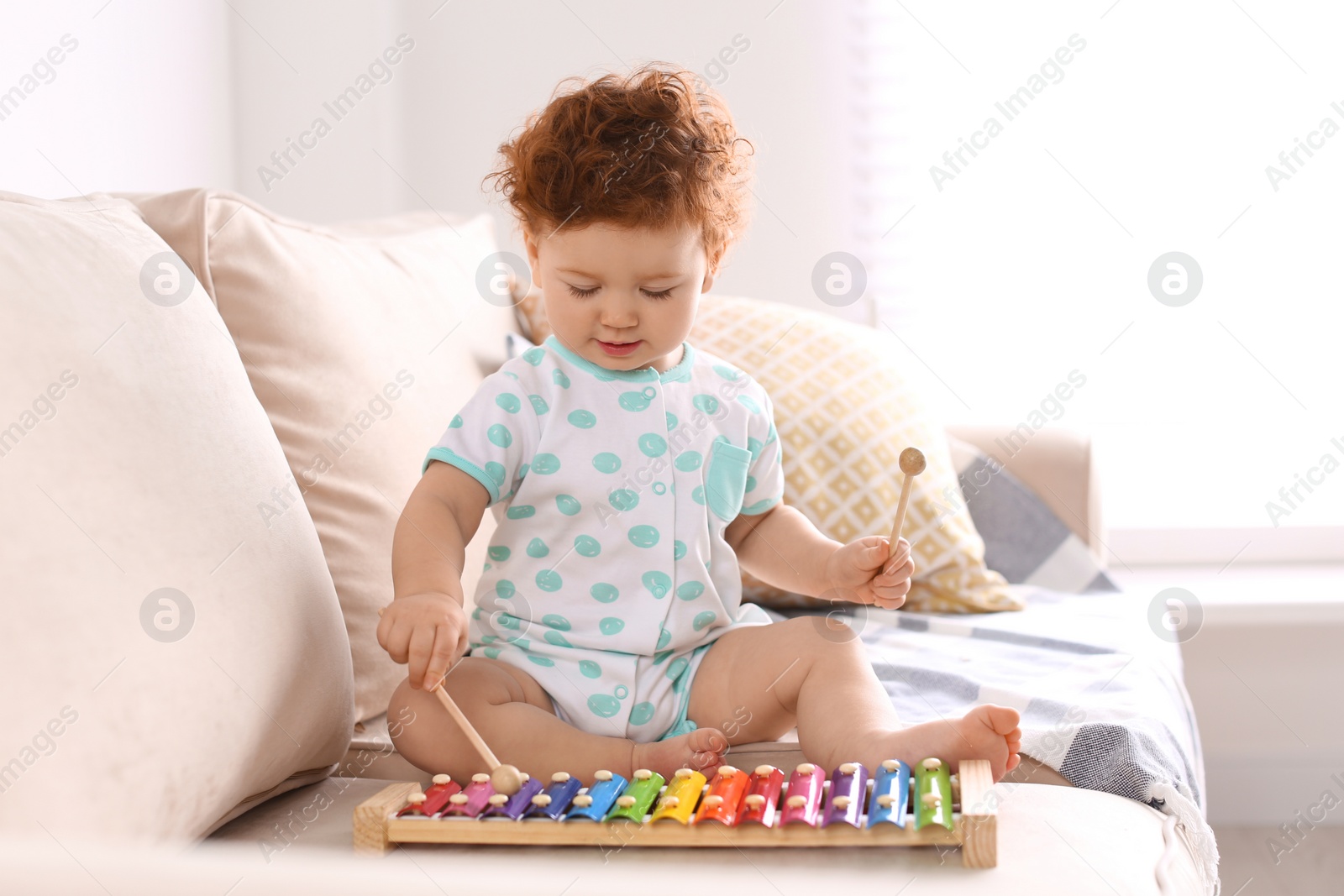 Photo of Cute little child playing with xylophone on sofa at home