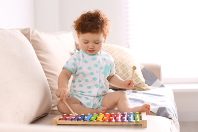 Cute little child playing with xylophone on sofa at home