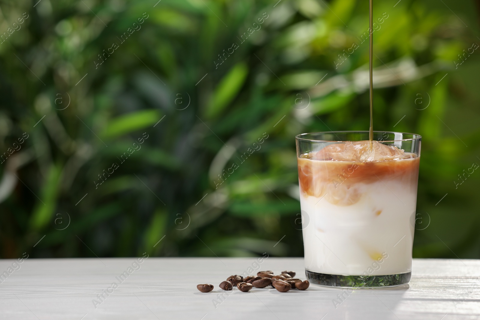 Photo of Making iced coffee at white wooden table outdoors, closeup. Space for text