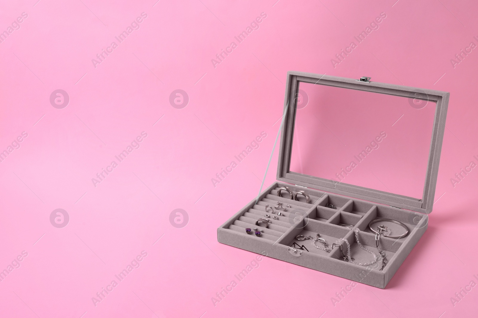 Photo of Jewelry box with many different silver accessories on pink background. Space for text