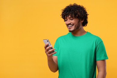 Photo of Handsome smiling man using smartphone on yellow background, space for text