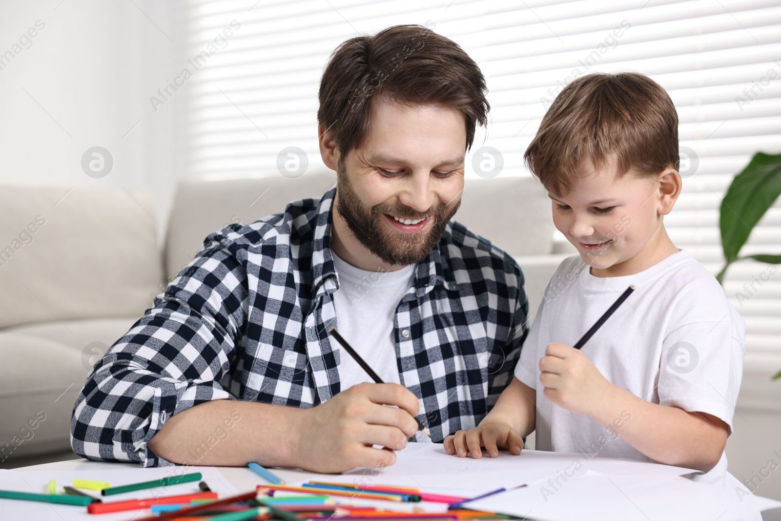 Photo of Happy dad and son drawing together at table indoors