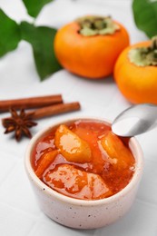Bowl of tasty persimmon jam and ingredients on white tiled table, above view
