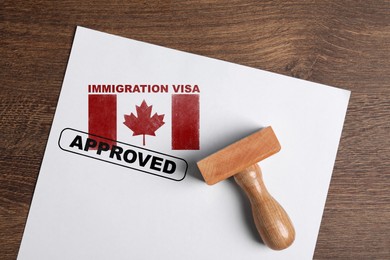 Document with approved immigration visa in Canada and stamp on wooden table, top view