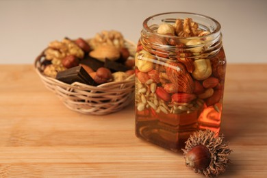 Photo of Different nuts and honey in jar, wicker basket with snacks on wooden table. Space for text