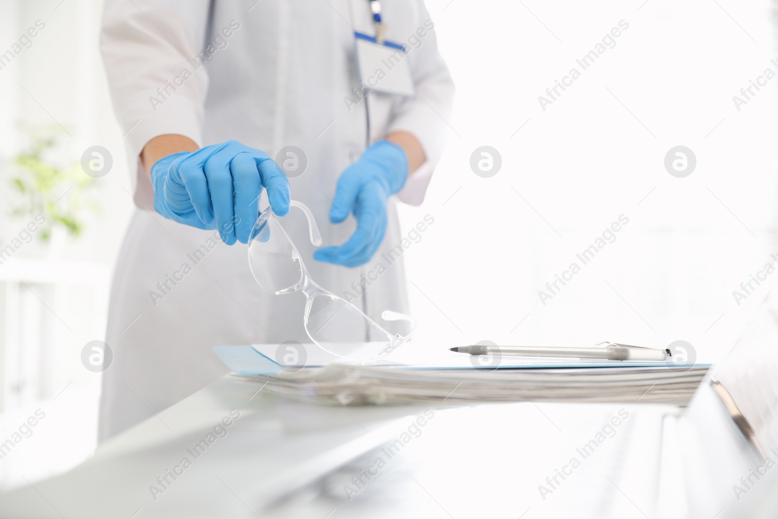 Photo of Doctor in medical gloves with glasses near table indoors, closeup