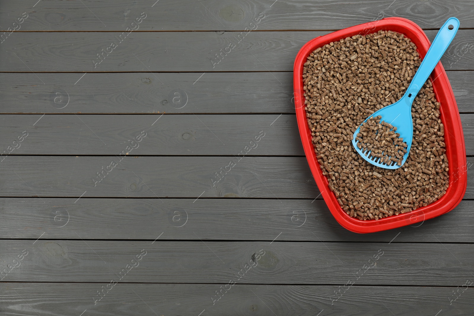 Photo of Cat litter tray with filler and scoop on grey wooden floor, top view. Space for text