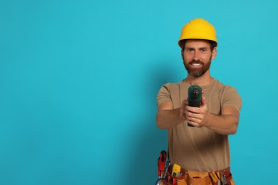 Professional builder in hard hat with tool belt and power drill on light blue background, space for text