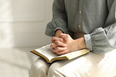 Photo of Religious woman praying over Bible indoors, closeup