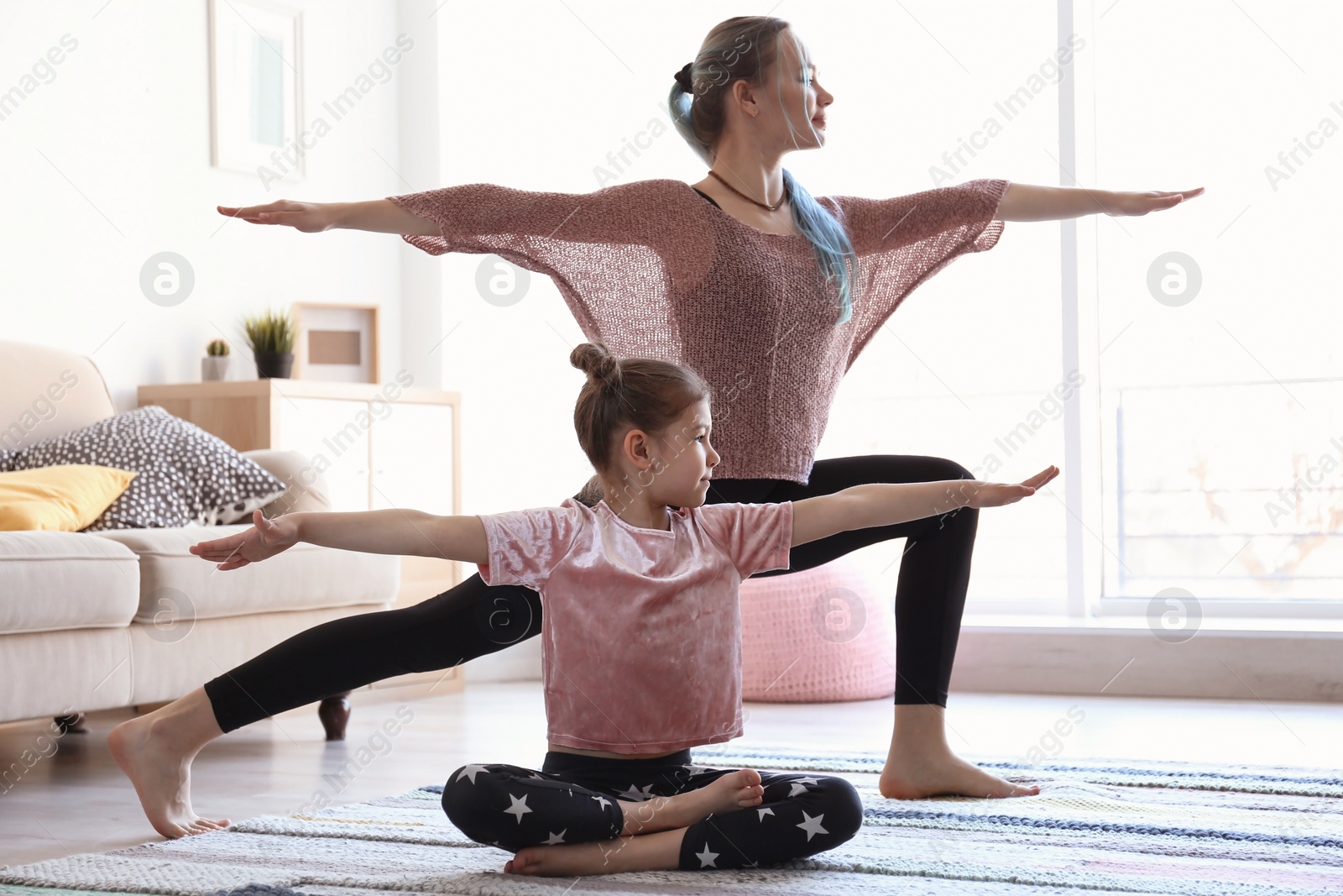 Photo of Young mother and her daughter practicing yoga at home