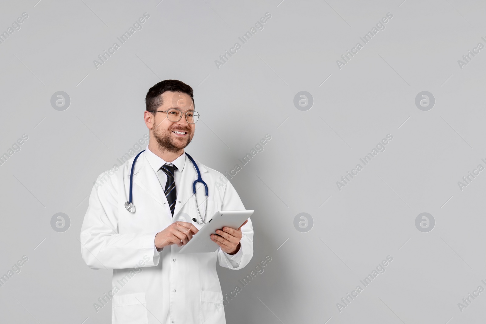 Photo of Portrait of smiling doctor with tablet on light grey background, space for text