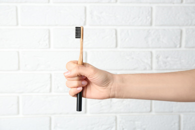 Photo of Woman holding bamboo toothbrush against white brick wall, closeup