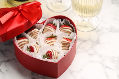 Delicious chocolate covered strawberries in heart shaped box and sparkling wine on white marble table. Space for text