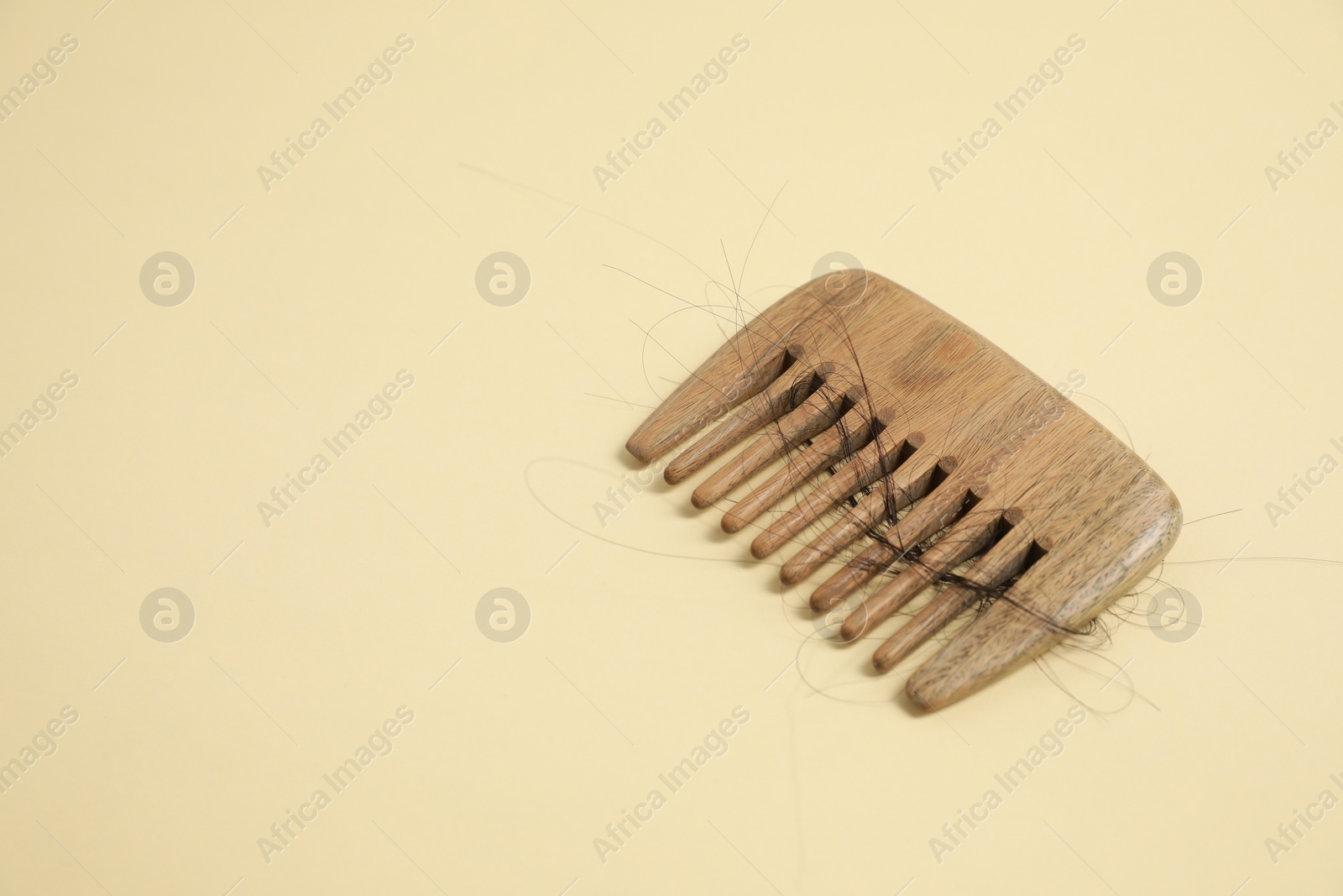 Photo of Wooden comb with lost hair on beige background. Space for text