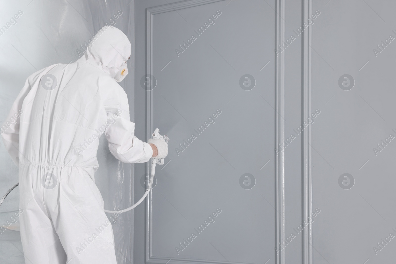 Photo of Decorator dyeing wall in grey color with spray paint, back view