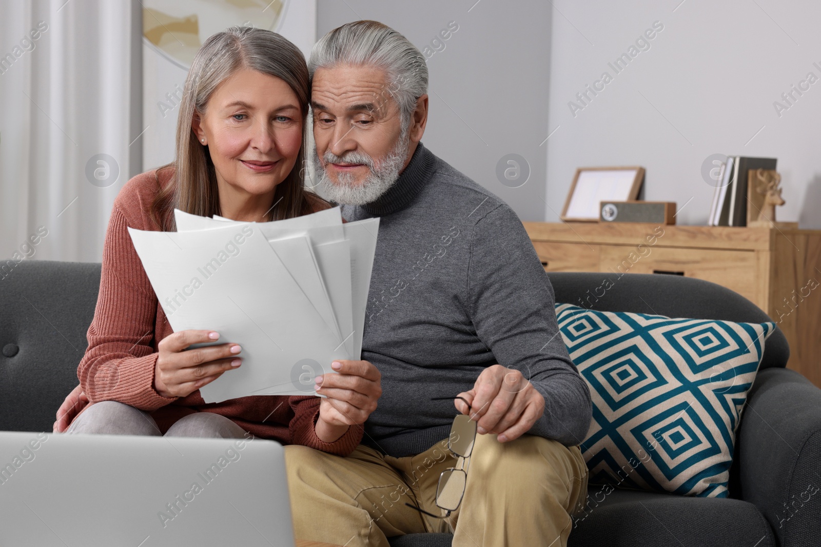 Photo of Elderly couple with papers and laptop discussing pension plan in room