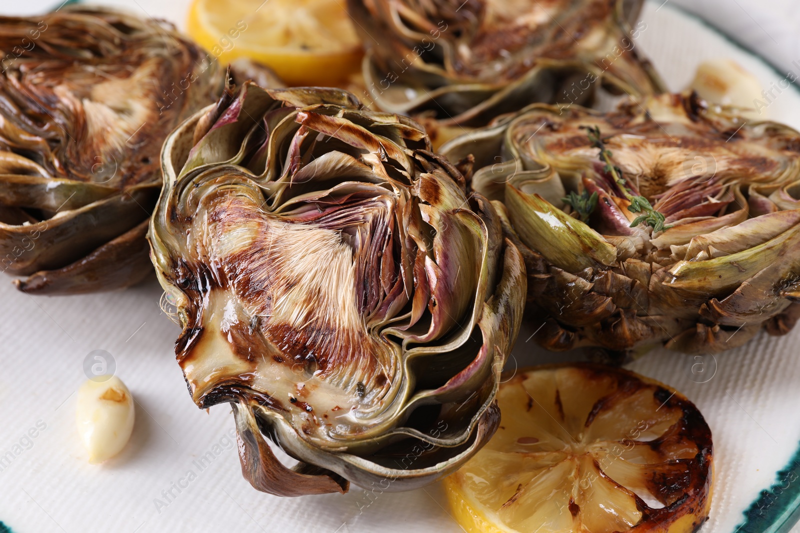 Photo of Tasty grilled artichokes and lemon slices on plate, closeup