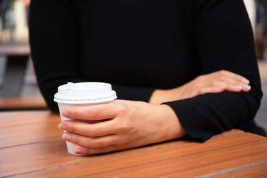 Woman with cardboard cup of coffee at table, closeup