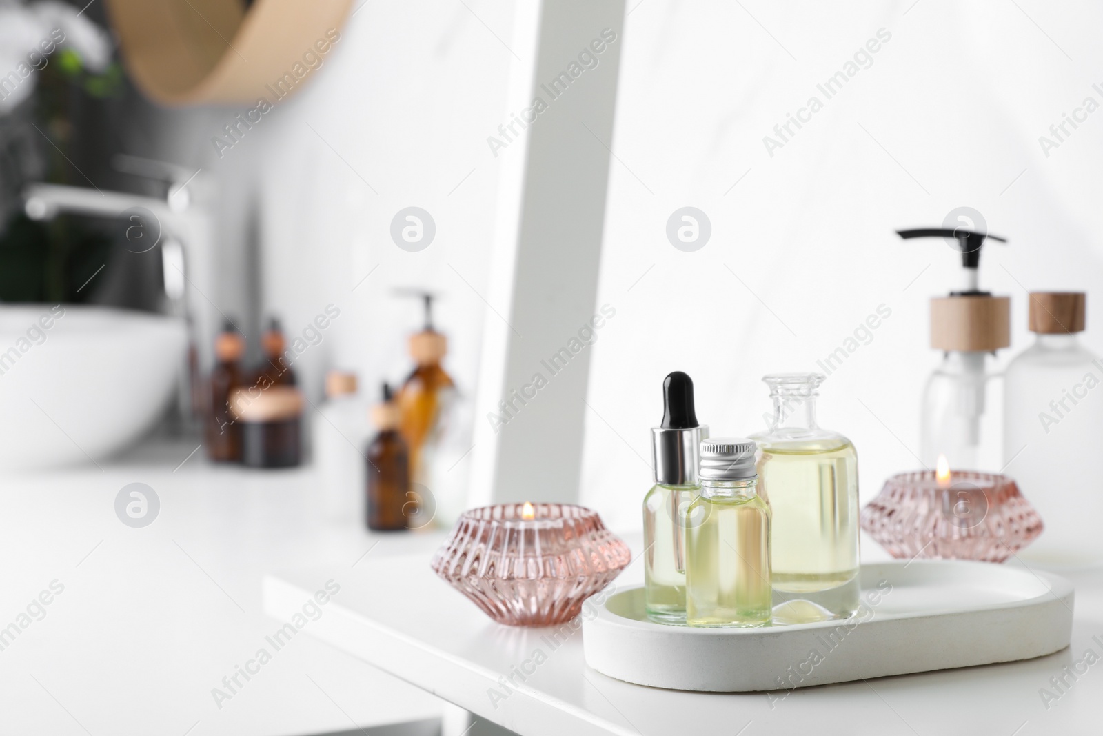 Photo of Essential oils and candles on white shelf in bathroom. Space for text