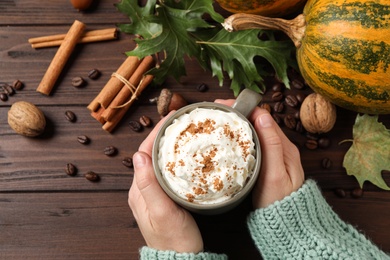 Woman with cup of tasty pumpkin spice latte at wooden table, top view