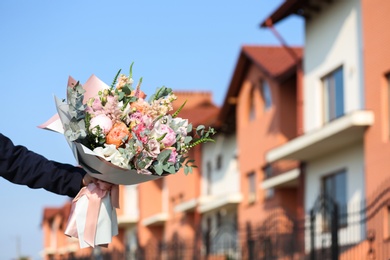 Photo of Man holding beautiful flower bouquet on street, closeup view. Space for text