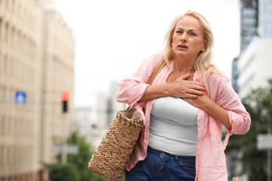 Mature woman suffering from heart attack outdoors. Space for text