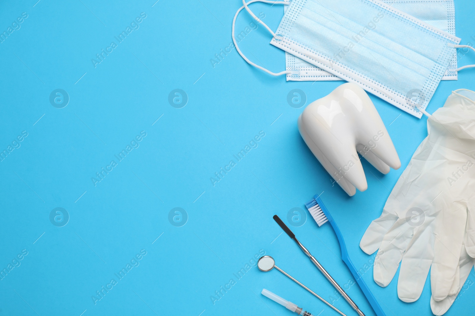 Photo of Tooth shaped holder, different dentist's tools, face masks and gloves on light blue background, flat lay. Space for text