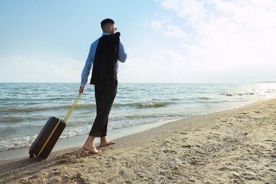 Photo of Businessman with suitcase walking on beach, low angle view. Business trip