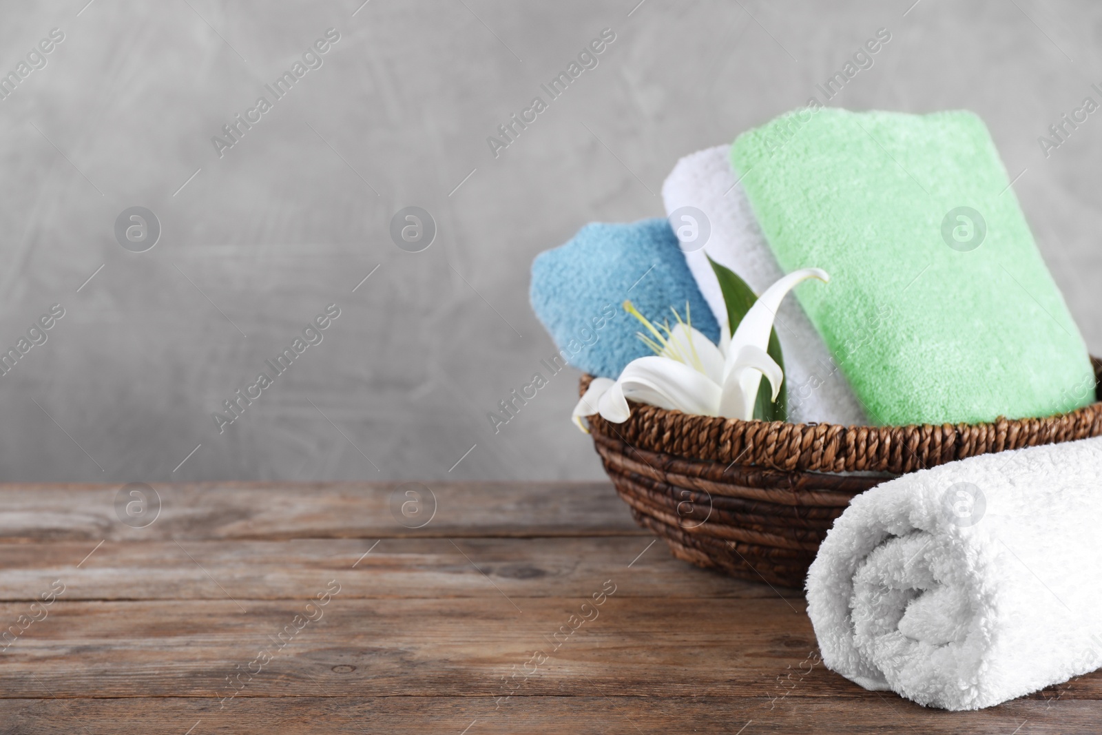 Photo of Wicker basket with folded bath towels and beautiful flower on wooden table. Space for text