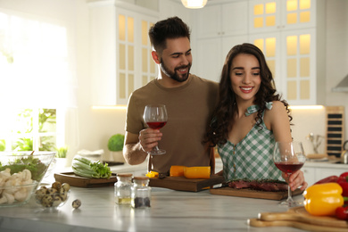 Lovely young couple with glasses of wine cooking together in kitchen