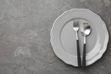 Stylish setting with cutlery and plate on grey textured table, top view. Space for text