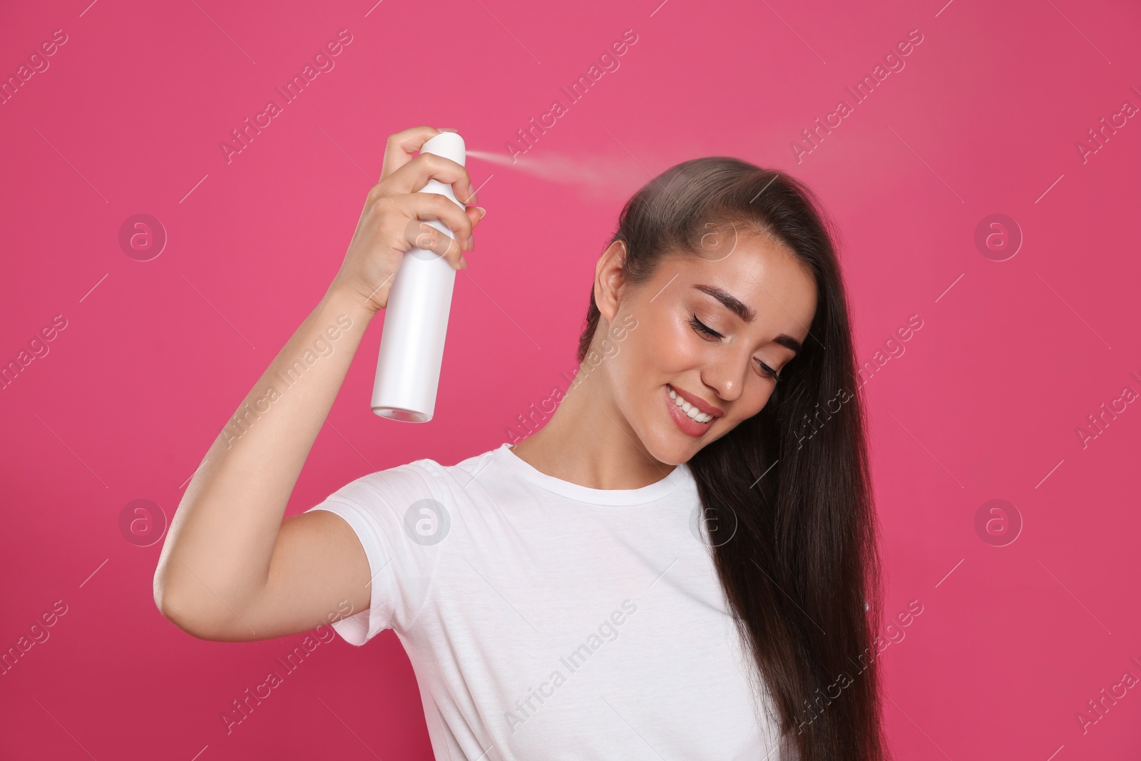 Photo of Young woman applying dry shampoo against pink background