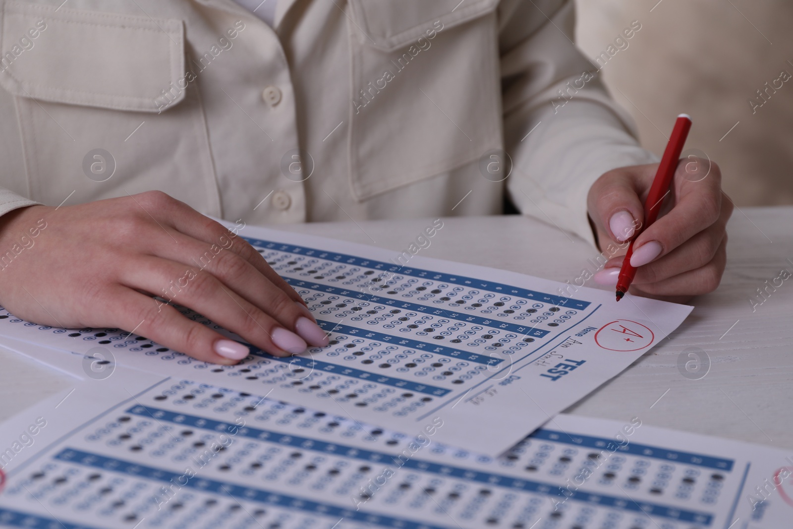 Photo of School grade. Teacher writing letter A with plus symbol on answer sheet at white table, closeup