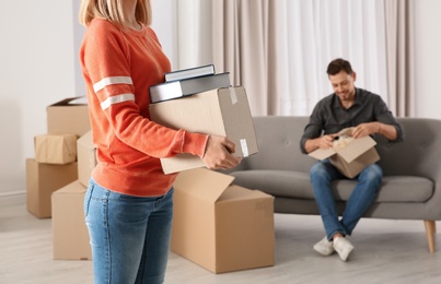 Photo of Woman carrying box full of books while man unpacking other in new house. Moving day