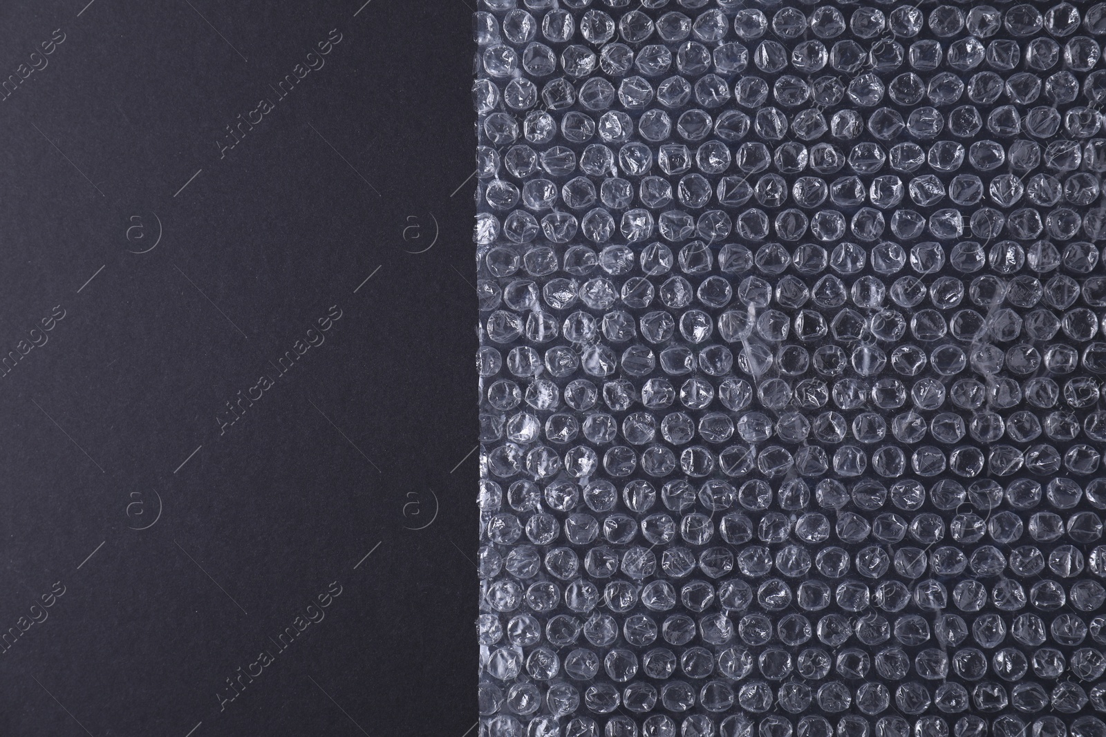 Photo of Transparent bubble wrap on black background, top view. Space for text