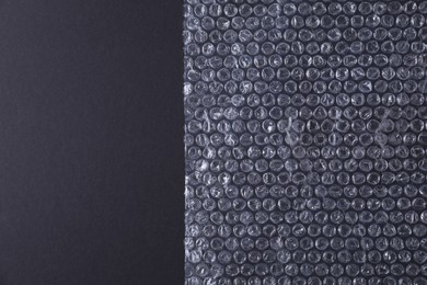 Photo of Transparent bubble wrap on black background, top view. Space for text